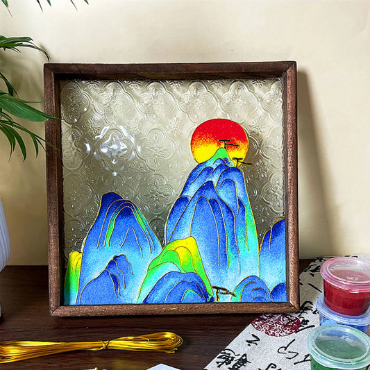 Framed cloisonne-inspired mountain and sunset design displayed beside craft supplies