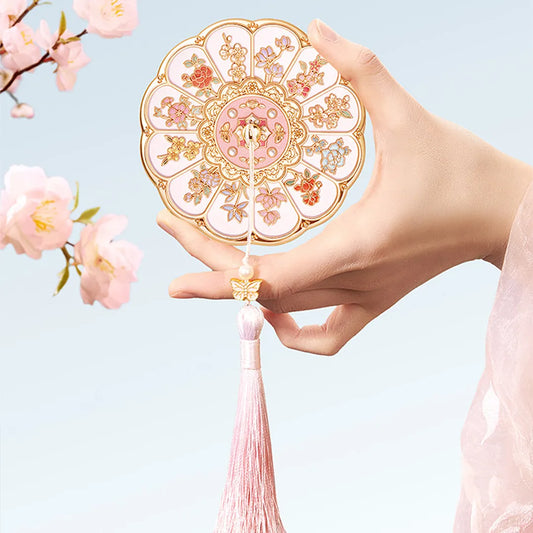 Hand holding the floral mirror by its handle against a pale blue background